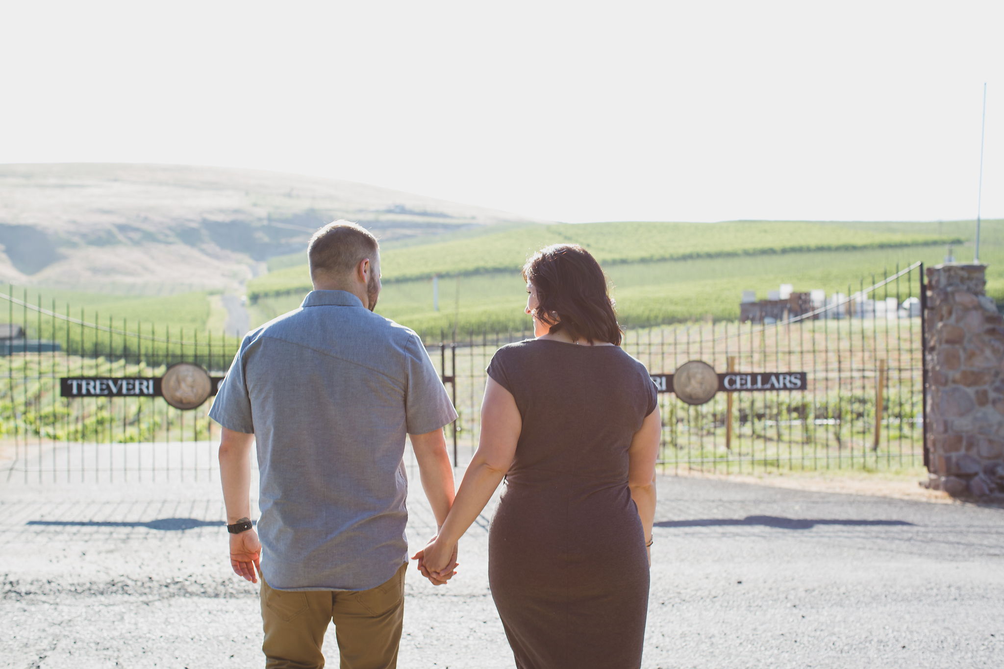 Engaged couple walking along a path with views of vineyards and orchards at Treveri Cellars in Yakima