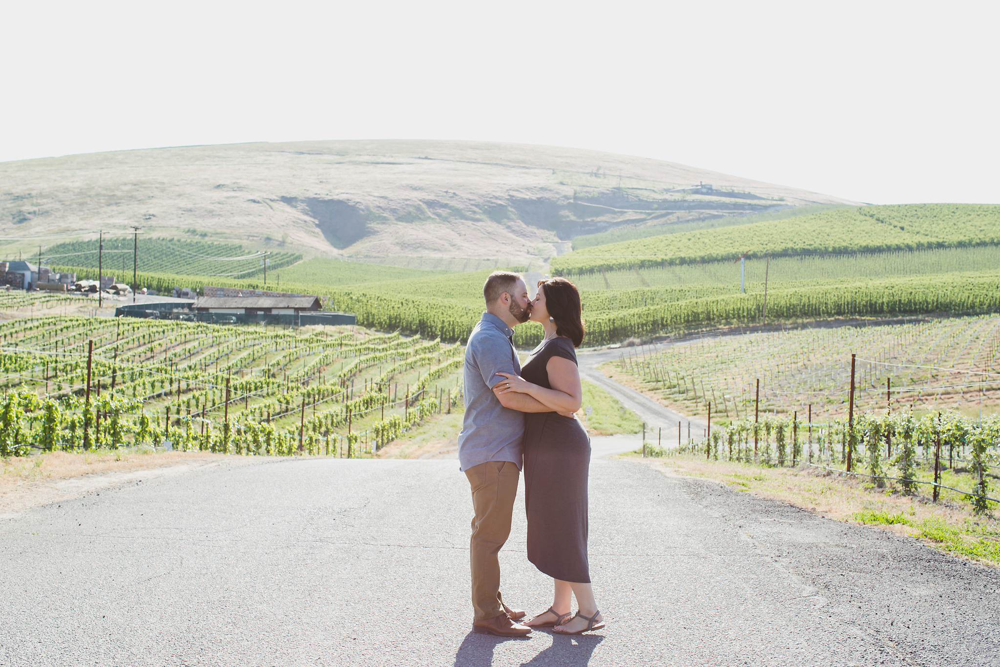Engaged couple kissing along a path with views of vineyards and orchards at Treveri Cellars in Yakima