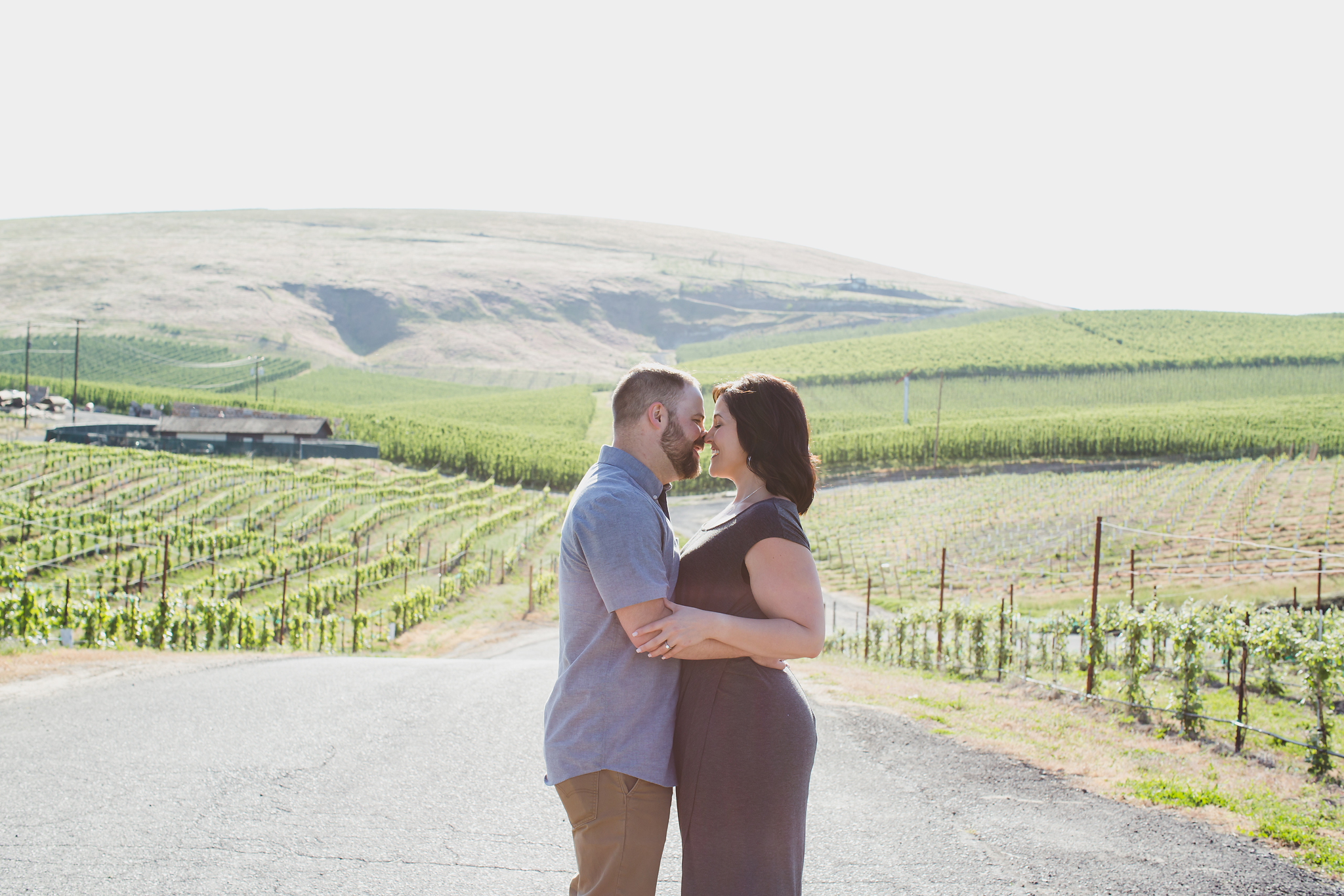 Engaged couple kissing along a path with views of vineyards and orchards at Treveri Cellars in Yakima