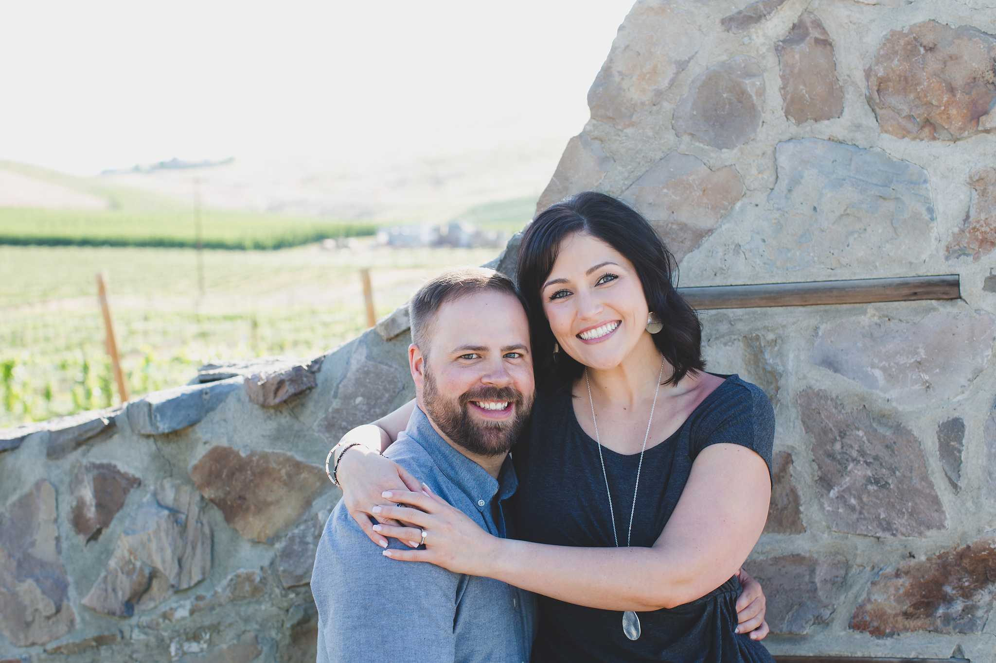 Engaged couple smiling in front of a stone gate at Treveri Cellars in Yakima