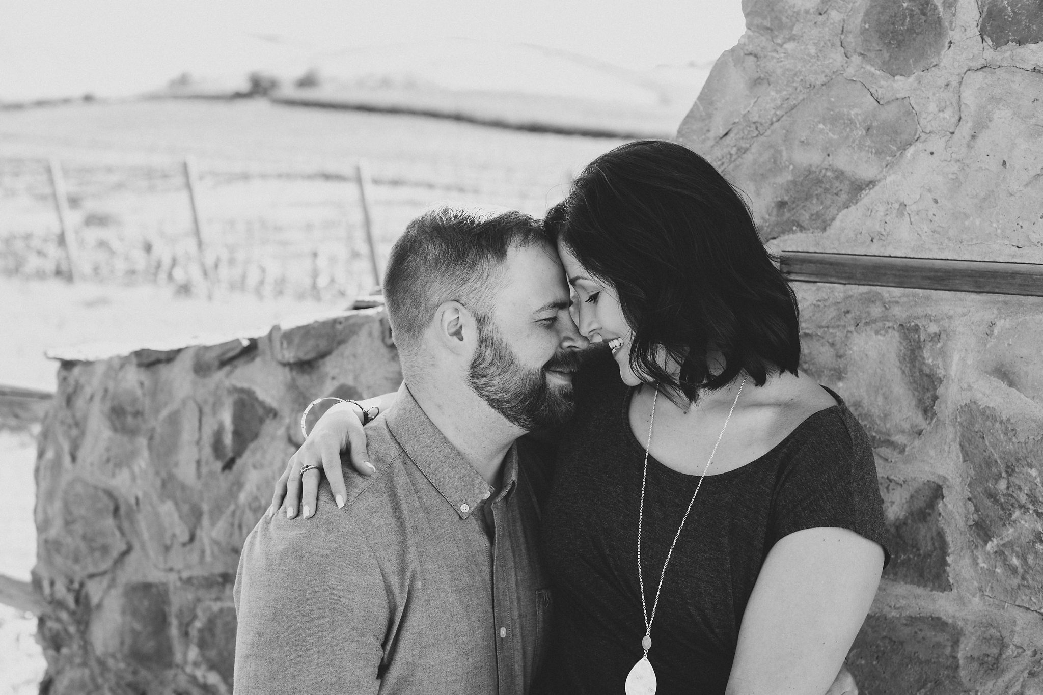 Engaged couple cuddling in front of a stone gate at Treveri Cellars in Yakima