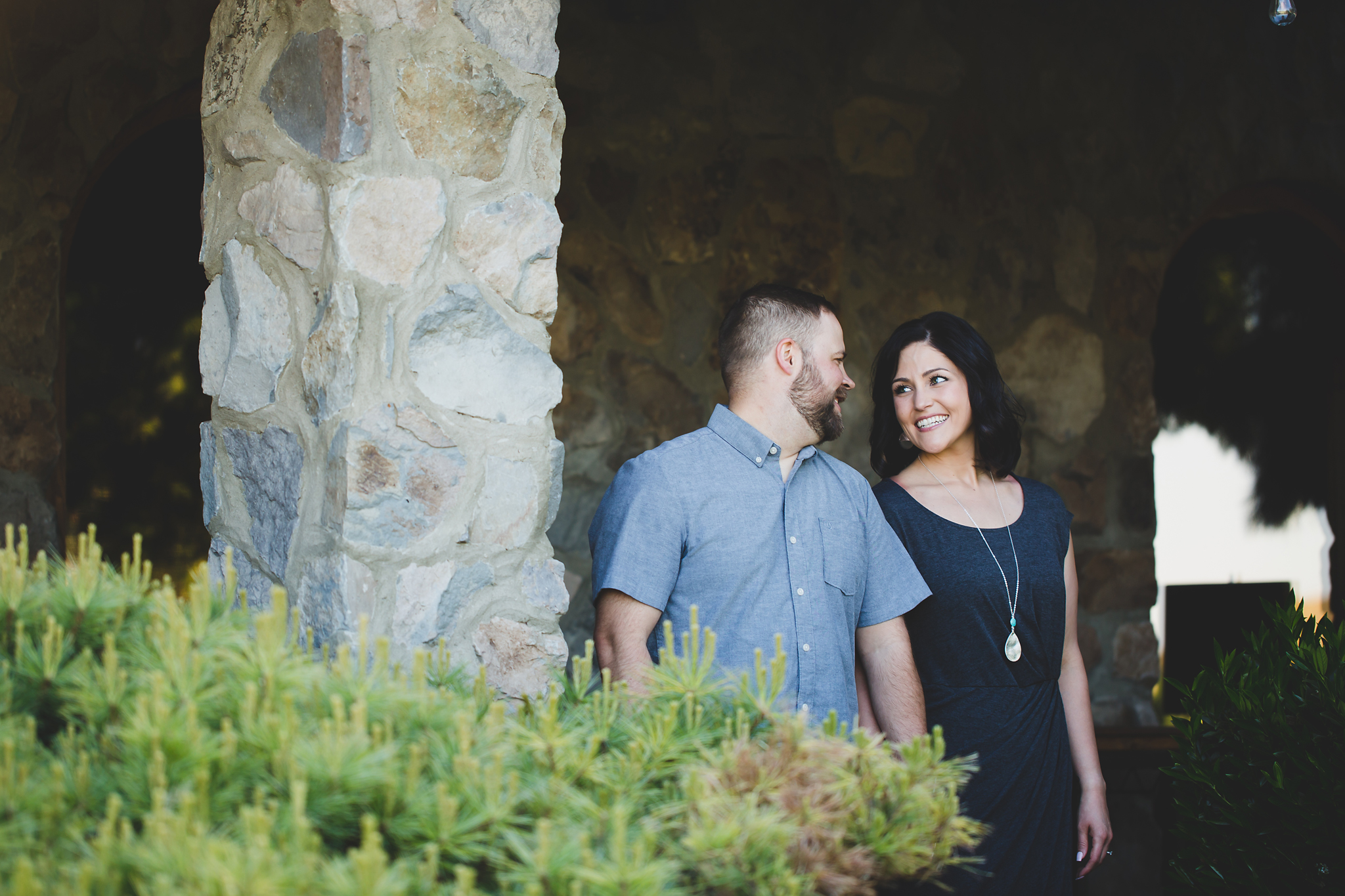 Engaged couple smiling at each other in front of a wall at Treveri Cellars in Yakima